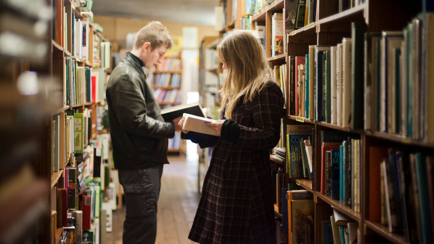 a standing man and woman reading a book in a library